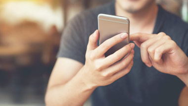 man on smartphone with blurred wooden background behind him
